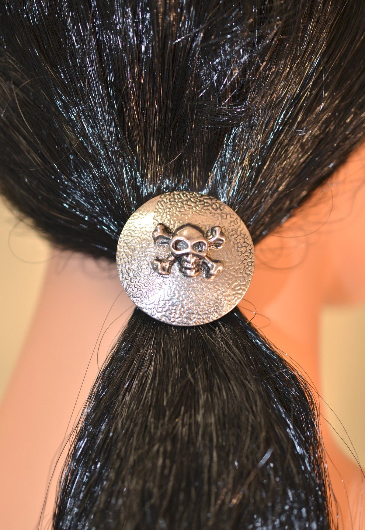 Silver skull and crossbones circle hair hook worn securing a ponytail, front view