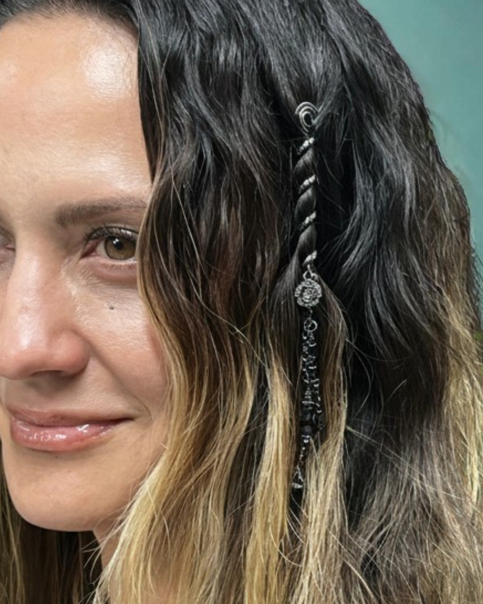 Woman with long, wavy hair featuring a decorative hairpiece against a light green background