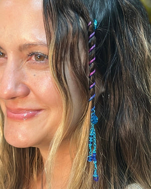 Close-up of a 4-inch rainbow Hair Twister spiral hair accessory with blue bead charm, worn in long wavy hair.