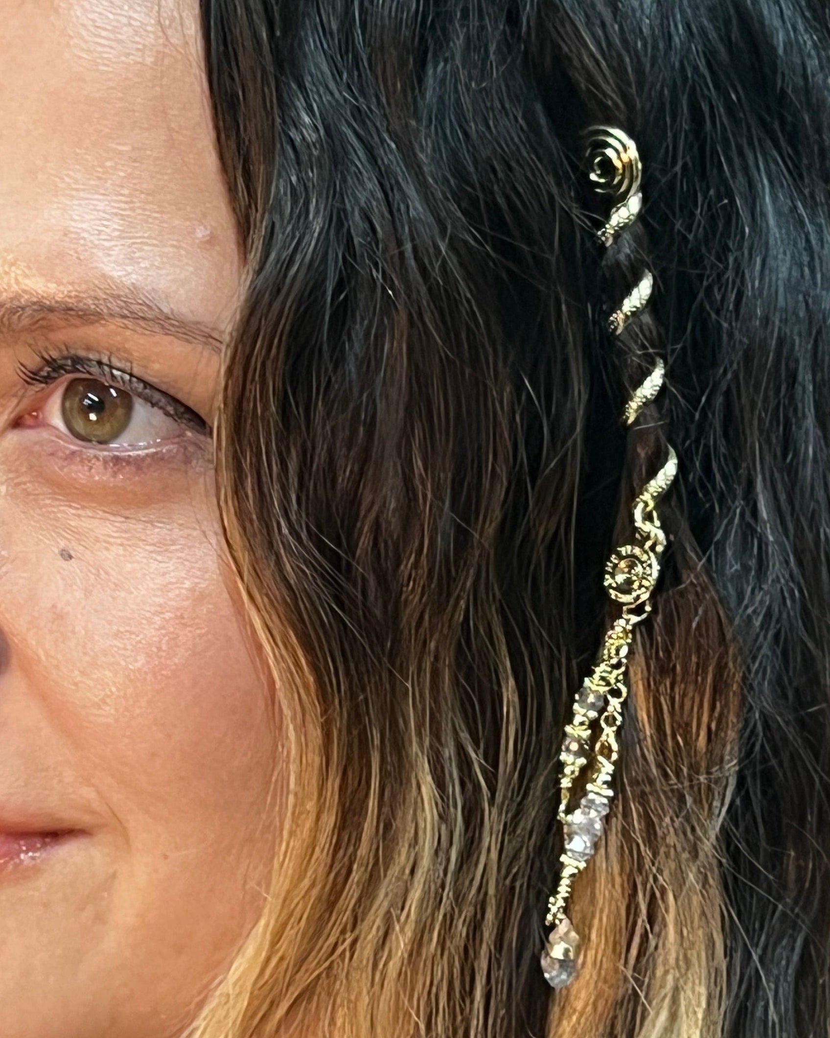 Woman wearing a 2-inch gold Mini Hair Twister spiral hair wrap with crystal charm accent, securing a small lock of hair for a boho-inspired hairstyle, close-up side view.