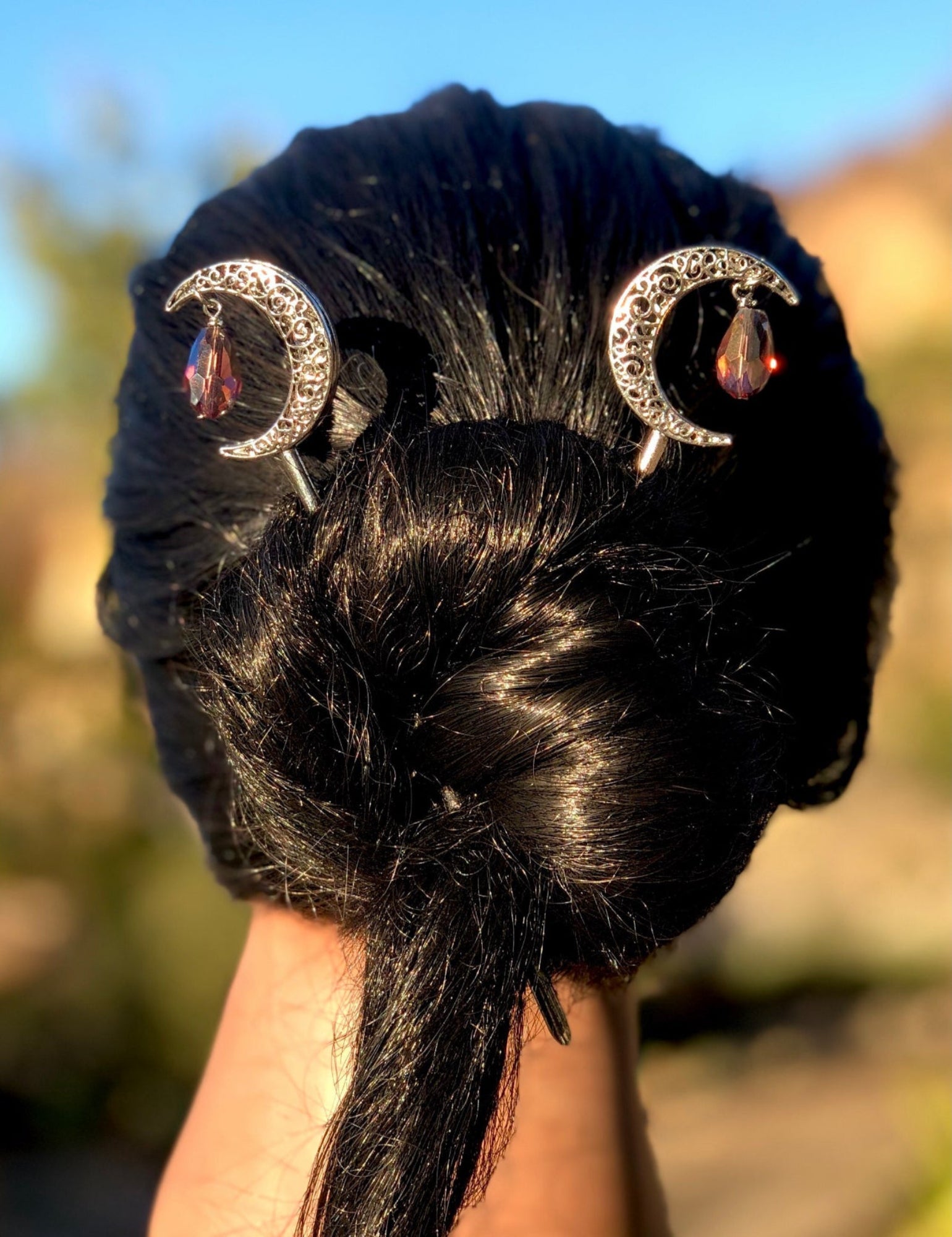 Silver crescent moon hair sticks with red gemstone details worn in a bun hairstyle, back view