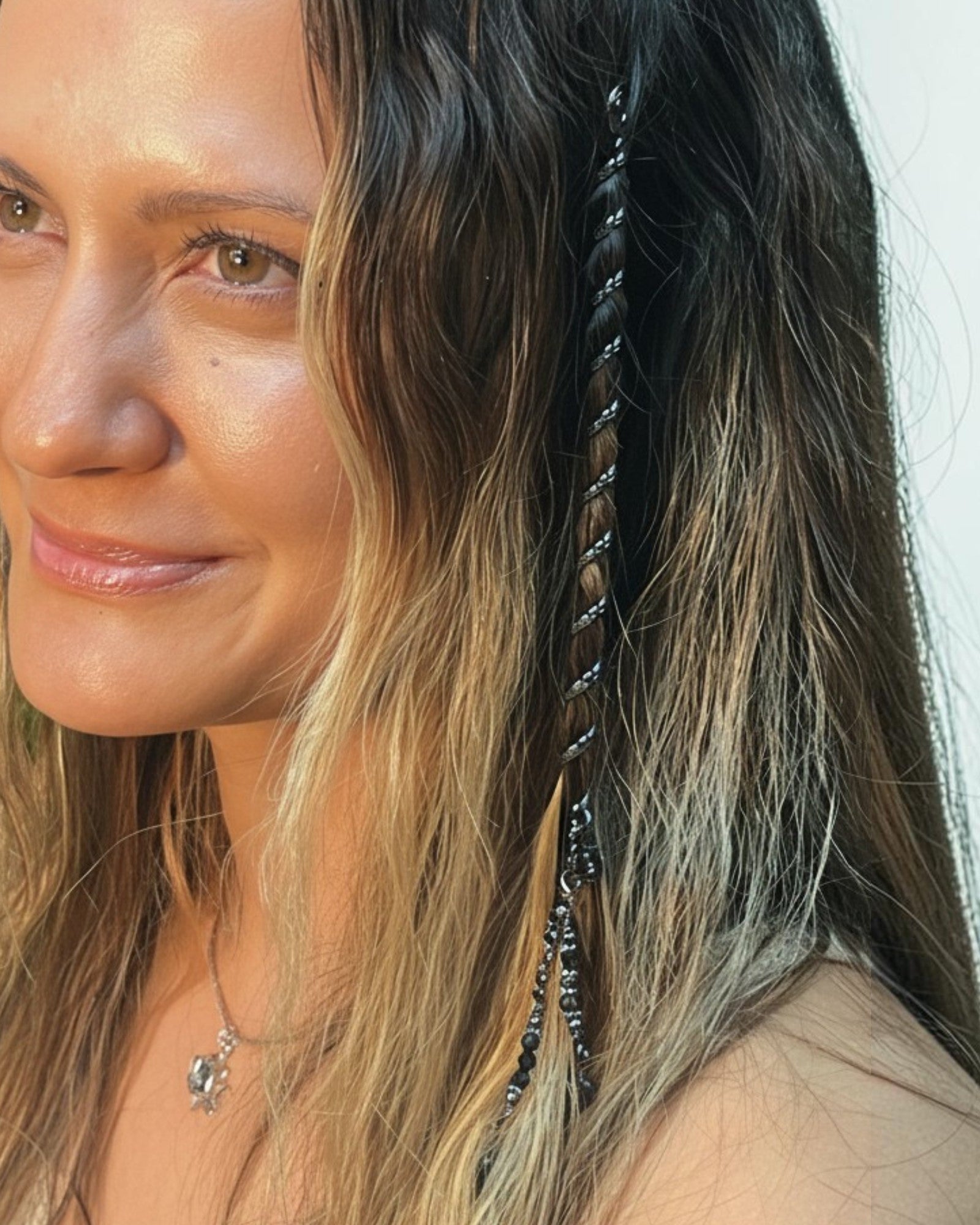 Woman wearing a 6-inch gun black Hair Twister spiral hair wrap with black gemstone bead charm, securing a section of hair for a boho-inspired hairstyle, side view.