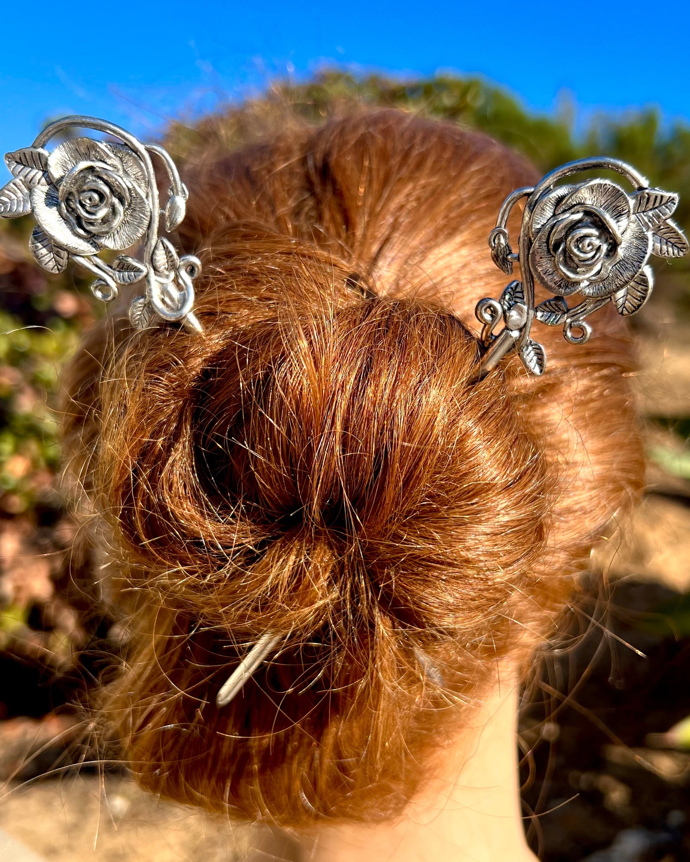 Model wearing silver rose hair sticks securing a bun hairstyle, elegant floral hair jewelry for women.