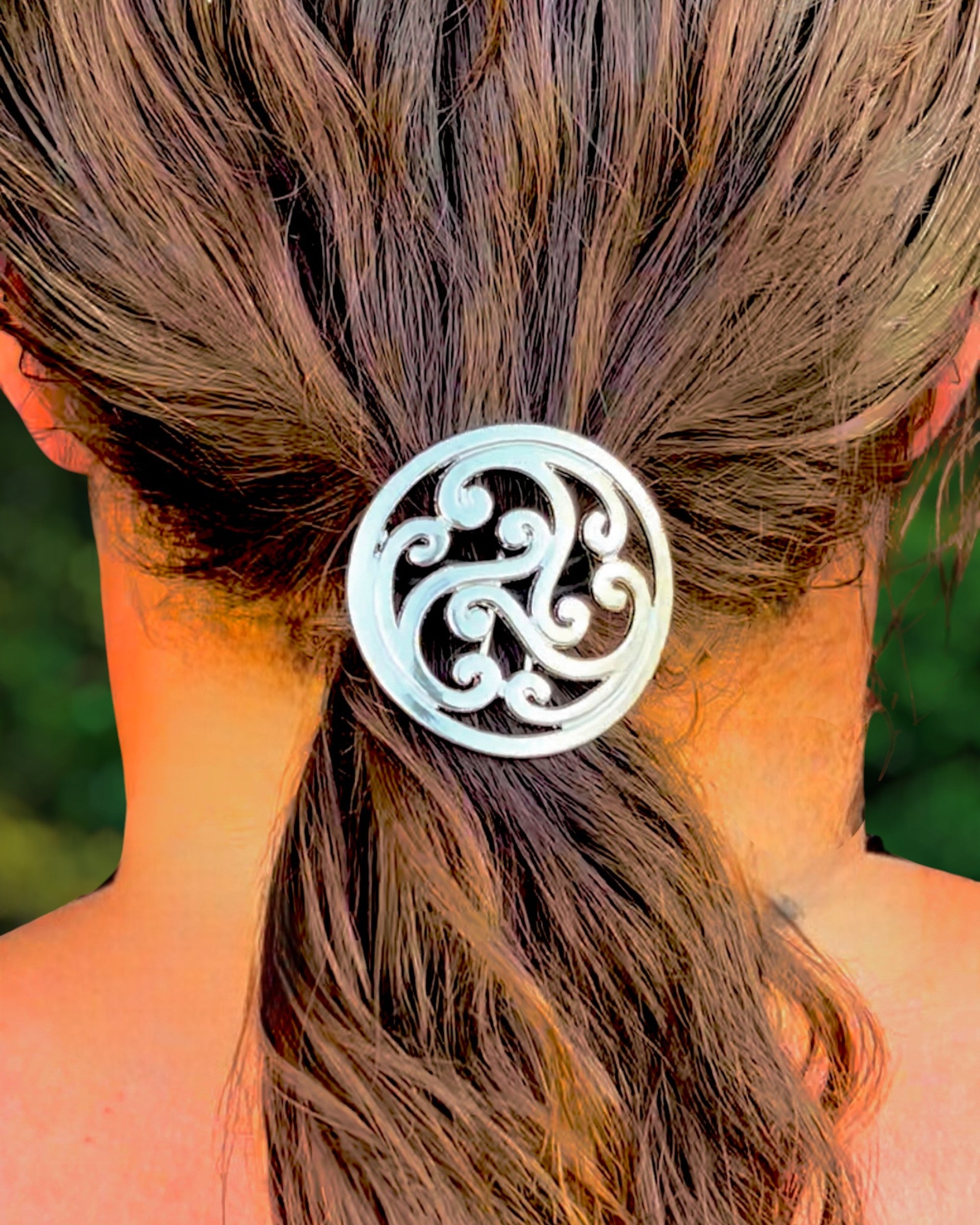 Decorative metal hair hook securing a low ponytail, worn in styled hair against a blurred green background