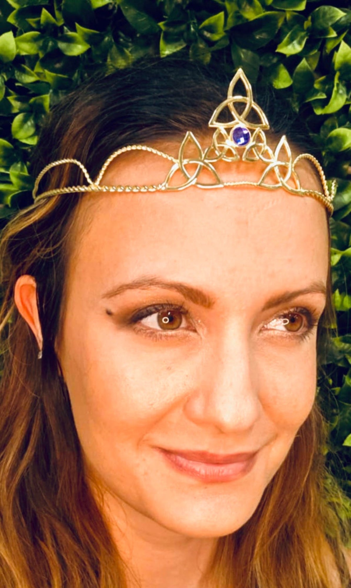 Model wearing gold triquetra wire crown with purple gemstone centerpiece, front view