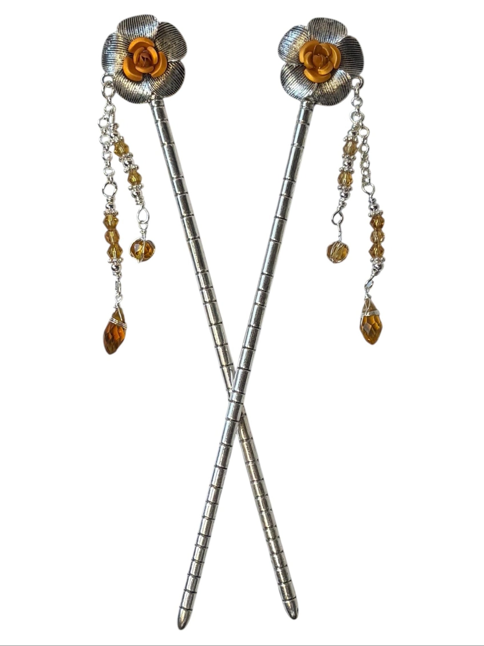 Pair of silver flower hair sticks with amber rose centers and amber crystal bead dangle chains, shown crossed on a white background to display the front view.