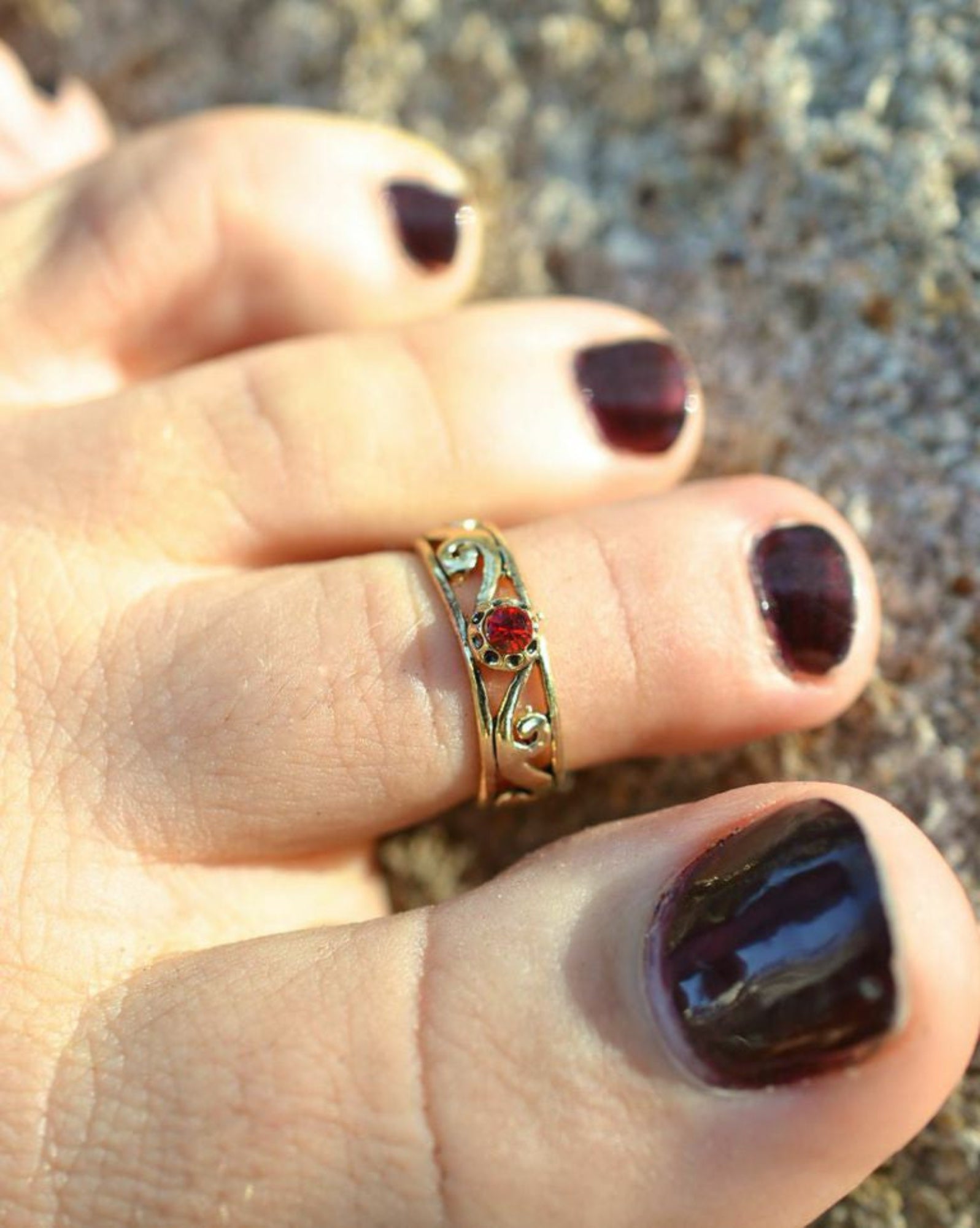 Model wearing spiral band toe ring with gold overlay and red stone