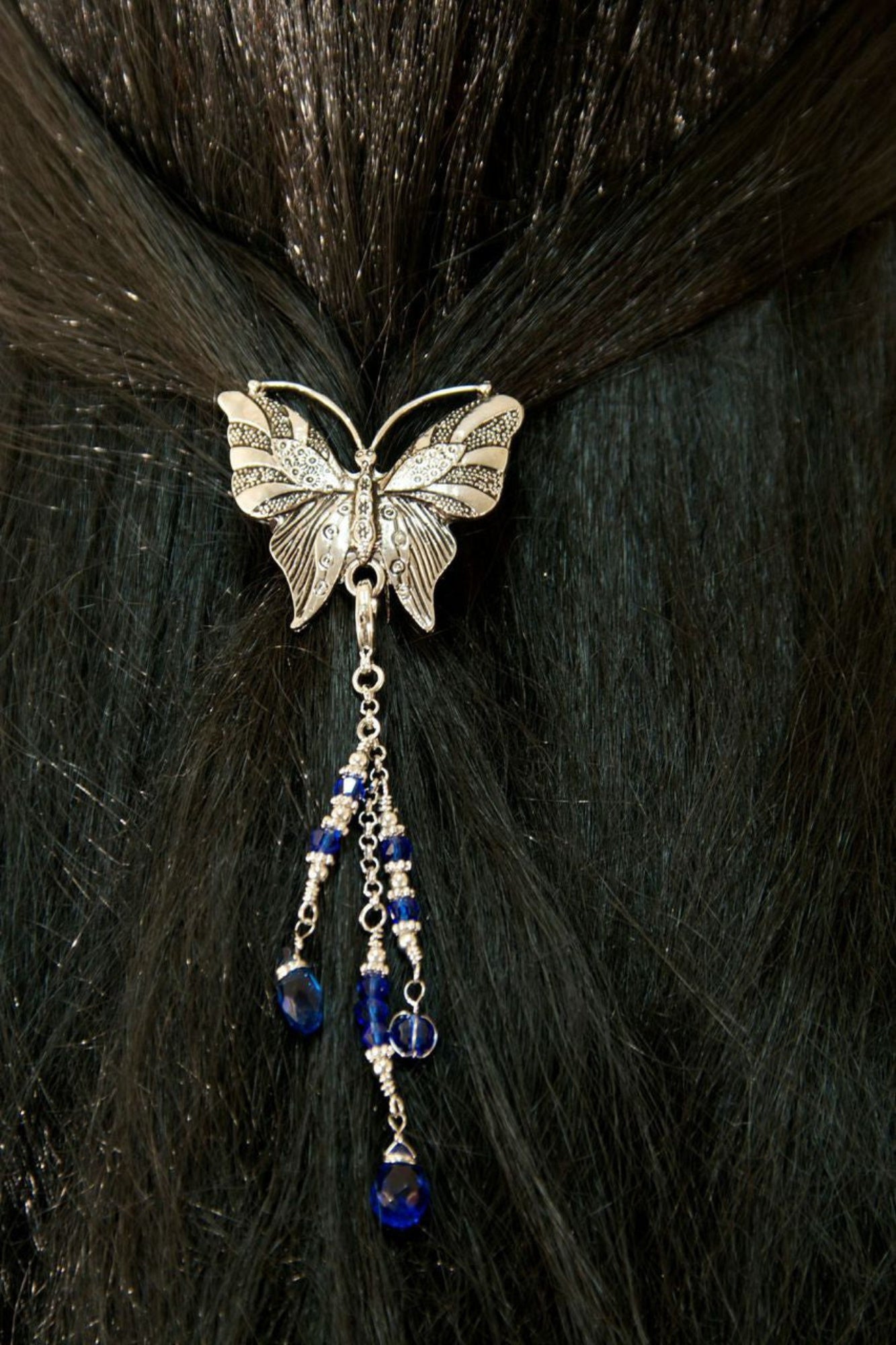 Silver butterfly hair hook ponytail holder with dangling blue crystal bead charms worn in dark ponytail, back view